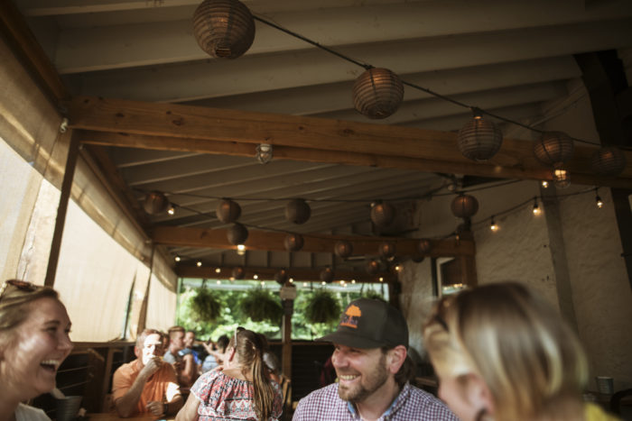 Group of people in a covered outdoor patio smiling and laughing with small lights strung overhead 